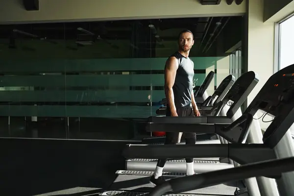 An athletic man in active wear stands confidently on a treadmill in a gym, focus and determination etched on his face. — Stock Photo