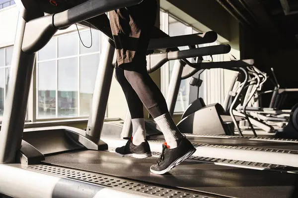 A man in active wear is running on a treadmill in a gym setting, with focused determination and a strong stride. — Stock Photo