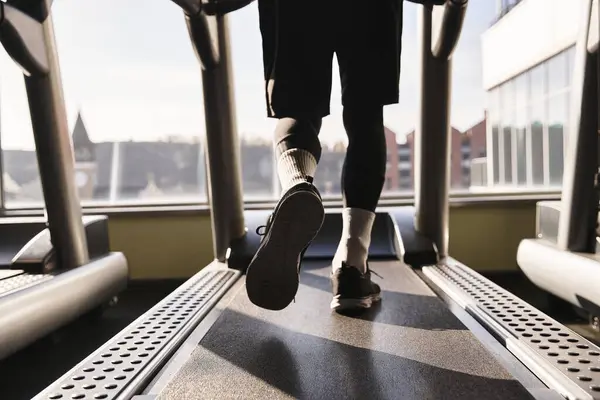 Un atlético en ropa deportiva camina enérgicamente en una cinta de correr en el gimnasio, centrándose en su rutina de entrenamiento. - foto de stock