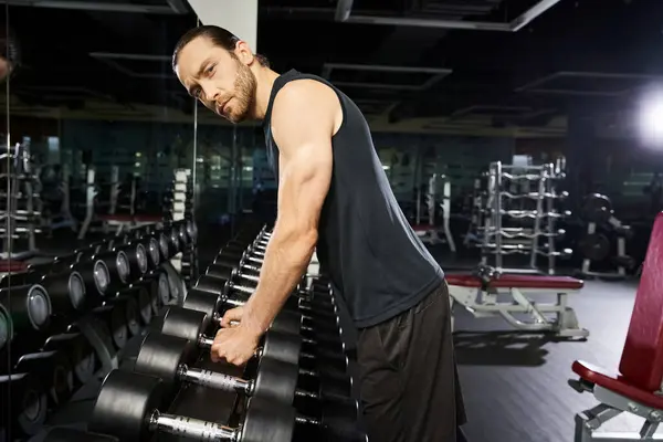 A fit man in activewear stands next to a row of dumbbells in a gym, preparing for an intense workout session. — Stock Photo
