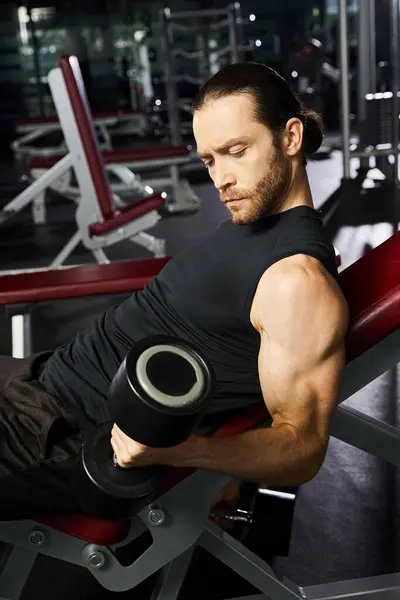 Ein athletischer Mann in aktiver Kleidung sitzt auf einer Bank und hält ein Paar Kurzhanteln, während er in einem Fitnessstudio trainiert. — Stockfoto