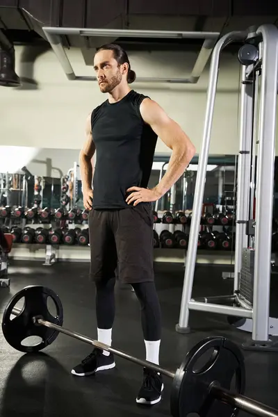 Un homme concentré et athlétique se tient devant un haltère dans un gymnase, prêt à lever et repousser ses limites dans une séance d'entraînement. — Photo de stock