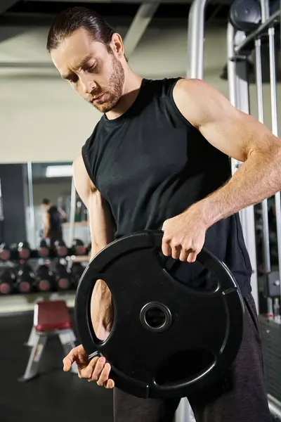 Un homme musclé en tenue d'entraînement tient une plaque noire à l'intérieur d'une salle de gym, montrant force et détermination. — Photo de stock
