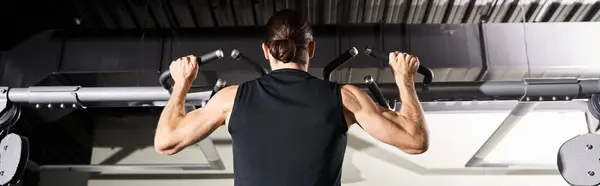 A determined man in a black shirt performs a pull-up, showcasing strength and perseverance in a gym setting. — Stock Photo