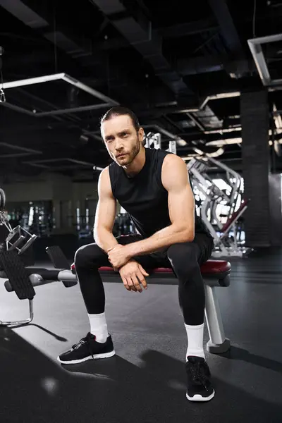 Ein athletischer Mann in aktiver Kleidung sitzt auf einer Gymnastikbank und ruht sich während seiner Trainingseinheit aus. — Stockfoto