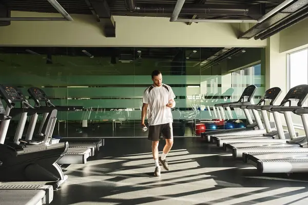A fit man in athletic attire walking near treadmills in a gym — Stock Photo