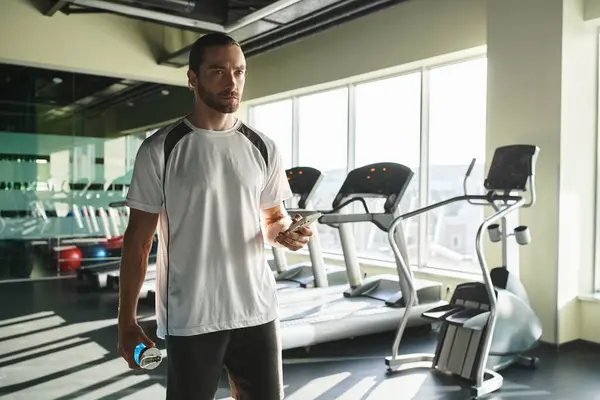 Ein athletischer Mann in aktiver Kleidung hält selbstbewusst eine Wasserflasche im Fitnessstudio. — Stockfoto