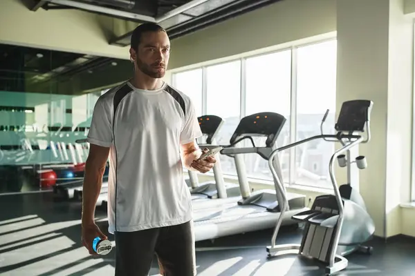 An athletic man in active wear confidently holds a water bottle in a gym setting. — Stock Photo