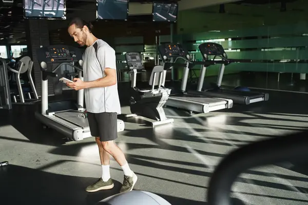 Ein muskulöser Mann in Aktivkleidung checkt sein Handy während einer Trainingspause im Fitnessstudio. — Stockfoto