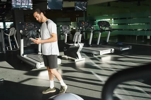 A muscular man in activewear checking his cell phone while taking a break from his workout routine at the gym. — Stock Photo