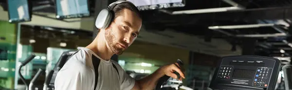 Un homme athlétique en tenue active utilise une machine tout en portant un casque pour une séance d'entraînement musicale améliorée. — Photo de stock
