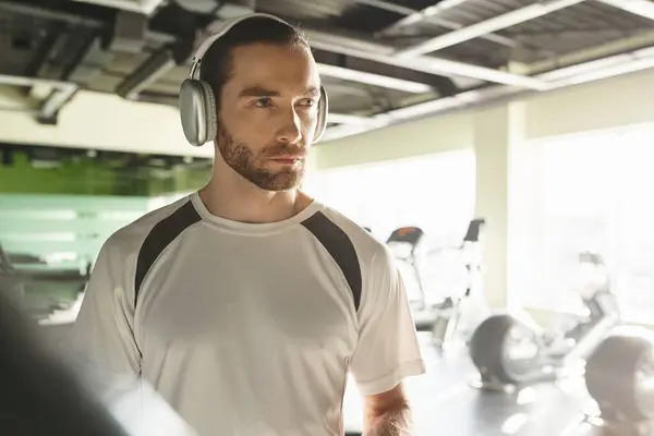 Um atlético de uso ativo ouve música em fones de ouvido enquanto faz exercício em um ginásio. — Fotografia de Stock