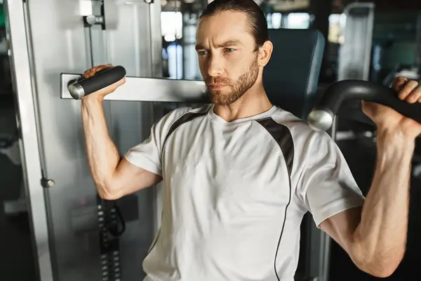 Un homme athlétique en tenue active, tenant une poignée sur une machine d'exercice tout en s'entraînant au gymnase. — Photo de stock