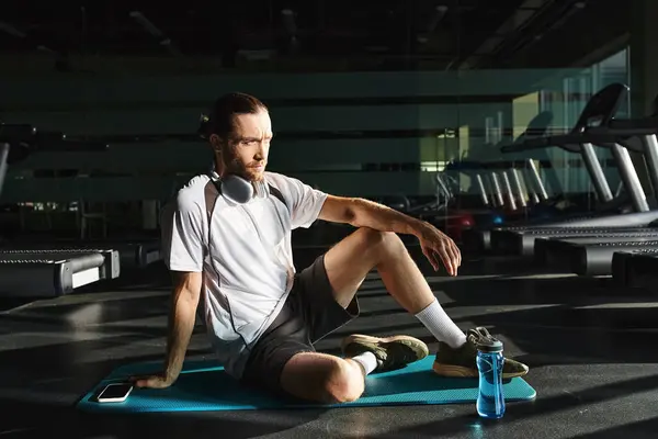 A fit man in activewear is sitting on a mat wearing headphones. — Stock Photo