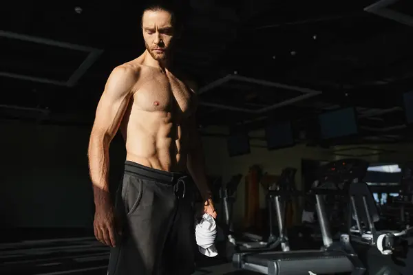 М'язистий чоловік, без сорочки, стоїть в спортзалі, демонструючи свою фізичну силу і відданість роботі. — стокове фото