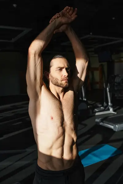 Homem sem camisa muscular em pé no ginásio com as mãos para cima, mostrando força e determinação na sessão de treino. — Fotografia de Stock