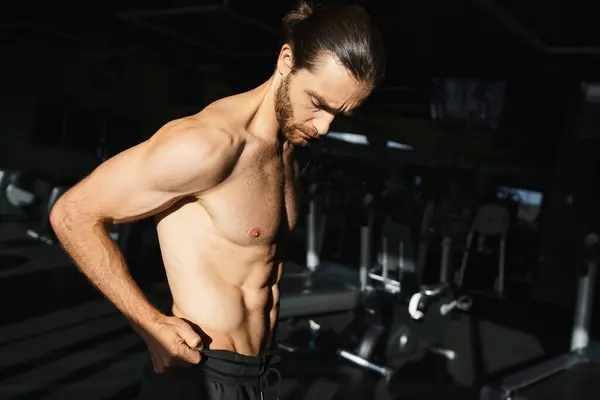 Um homem sem camisa fica confiante na frente de uma máquina de ginástica, mostrando seu físico muscular. — Fotografia de Stock