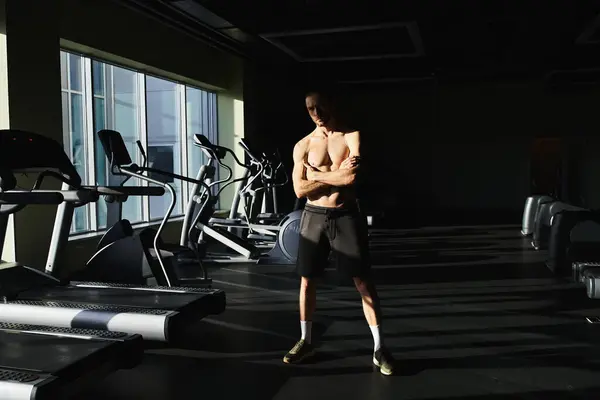 A muscular man without a shirt standing confidently in front of a row of treadmills in a gym. — Stock Photo