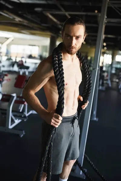 Shirtless man showcasing muscular physique while gripping a rope in gym. — Stock Photo