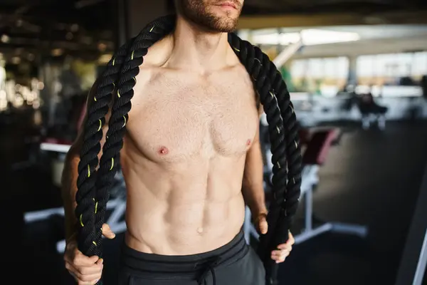 Um homem musculoso sem camisa segura ferozmente uma corda, mostrando sua força e determinação durante uma sessão de treino no ginásio. — Fotografia de Stock