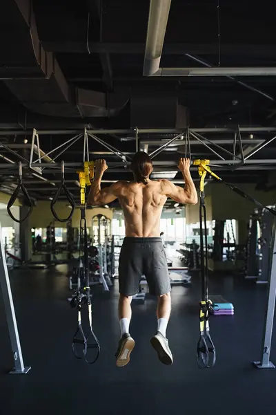 Muscular man without shirt doing pull ups on a bar in a gym. — Stock Photo