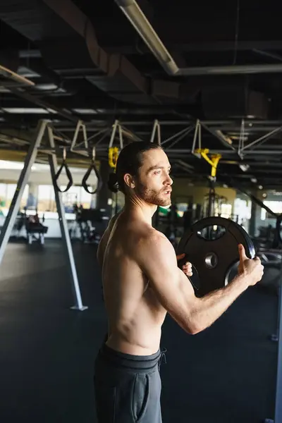 Hombre sin camisa mostrando su fuerza mientras sostiene una placa de peso en un entorno de gimnasio. - foto de stock