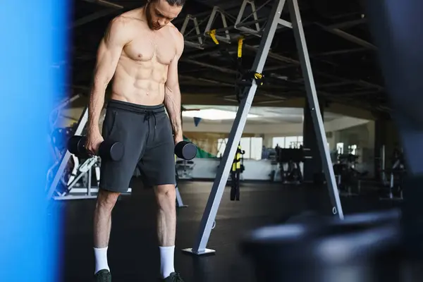 Человек без рубашки, мускулистый поднимает гантели в тренажерном зале, демонстрируя силу и приверженность к тренировке.. — стоковое фото