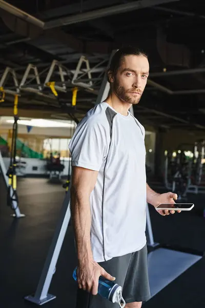 A muscular man hydrating with a water bottle in a gym while working out. — Stock Photo