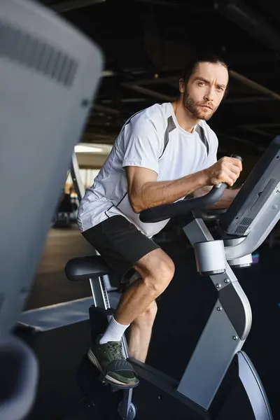 Um homem musculoso energeticamente pedalando uma bicicleta estacionária em um ginásio. — Fotografia de Stock