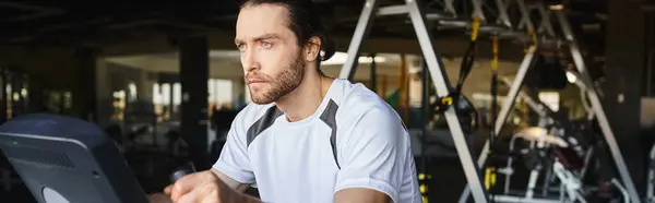 Un hombre musculoso con una camisa blanca está en bicicleta en un gimnasio. - foto de stock