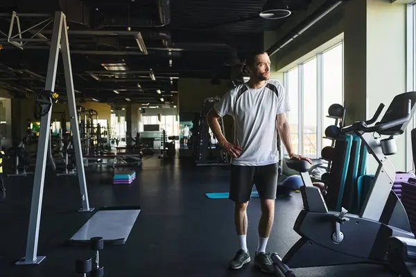 Un uomo muscoloso in piedi in una palestra circondato da un rack di attrezzature per l'esercizio. — Foto stock