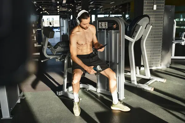 A shirtless man sitting on a bench, engrossed in his cell phone and headphones — Stock Photo