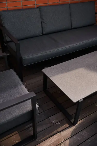 Un elegante sofá y modernos muebles de mesa colocados en una cubierta de madera envejecida en un tranquilo espacio al aire libre - foto de stock