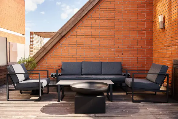 Uma configuração aconchegante de um sofá e cadeiras em um deck de madeira, cercado pela natureza, perfeito para relaxar ou entreter ao ar livre — Fotografia de Stock