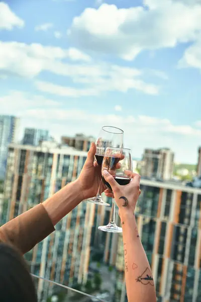 Two people clink wine glasses, celebrating, in front of a stunning city skyline at night, the lights creating a magical backdrop — Stock Photo