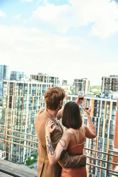 Um jovem casal, copos levantados, brindes à vida em meio ao pano de fundo de um horizonte movimentado da cidade. — Fotografia de Stock