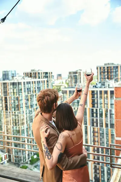 A man and woman stand confidently on the edge of a towering building, embracing the cityscape spread out before them — Stock Photo