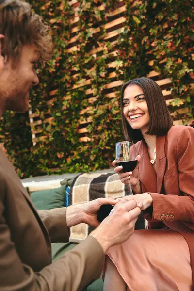 Um homem de terno segurando um copo de vinho ao lado de uma mulher em um vestido de cocktail, compartilhando um momento de conexão e intimidade — Fotografia de Stock