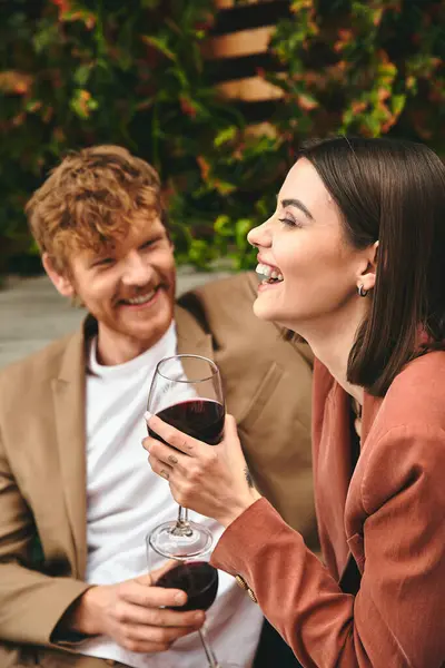 Un hombre y una mujer se sientan lado a lado, tintineando copas de vino en un gesto romántico - foto de stock
