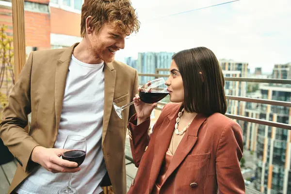 Um homem e uma mulher elegantes de pé juntos, a mulher segurando um copo de vinho — Fotografia de Stock