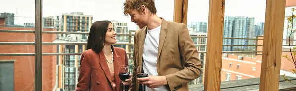 Un homme et une femme se tiennent ensemble, elle tient un verre de vin. Le couple semble sophistiqué et détendu dans leur environnement — Photo de stock