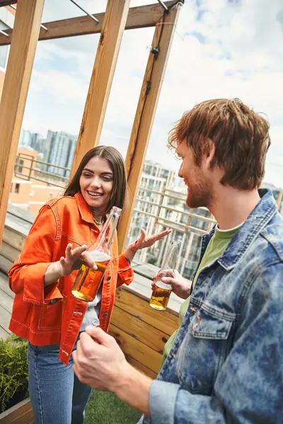 Dois amigos compartilham um momento lúdico com bebidas na mão, cercados por vistas da paisagem urbana de um telhado — Fotografia de Stock