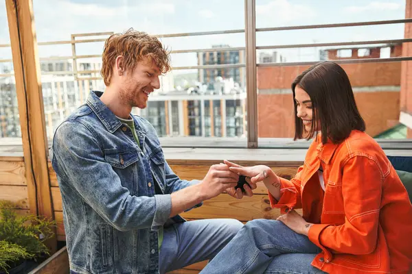 A man and woman sitting atop a window sill, lost in conversation, silhouetted against the glowing city lights at dusk — Stock Photo