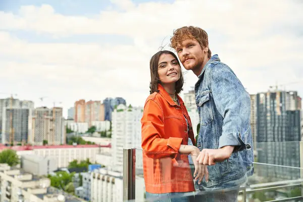 Un homme et une femme se tiennent côte à côte sur un balcon donnant sur les toits de la ville — Photo de stock