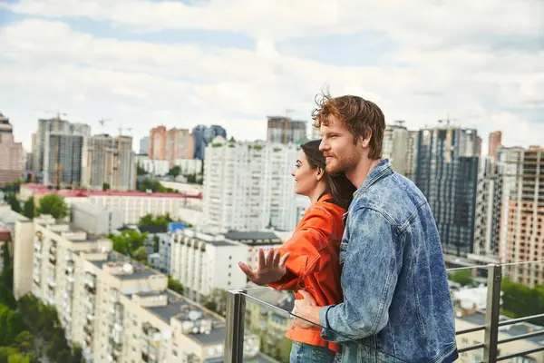 A man and woman stand on a balcony, gazing at a sprawling city below them under the night sky — Stock Photo