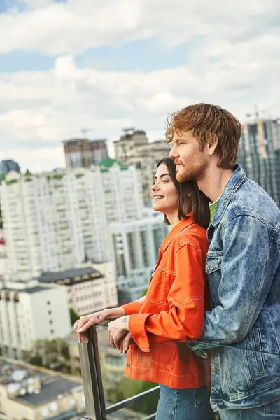 Ein Mann und eine Frau stehen auf einem Balkon und starren auf die darunter liegenden Lichter der Stadt, verloren in der Schönheit der nächtlichen Stadtlandschaft. — Stockfoto