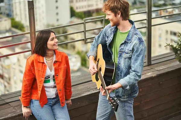 A man strums a guitar while a woman sits beside him, captivated by the music. Their connection is palpable in the intimate setting — Stock Photo