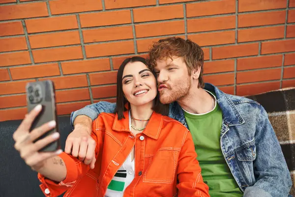Un hombre y una mujer sonriendo, sosteniendo un teléfono celular, tomando una selfie juntos en un feliz momento de conexión y amor - foto de stock