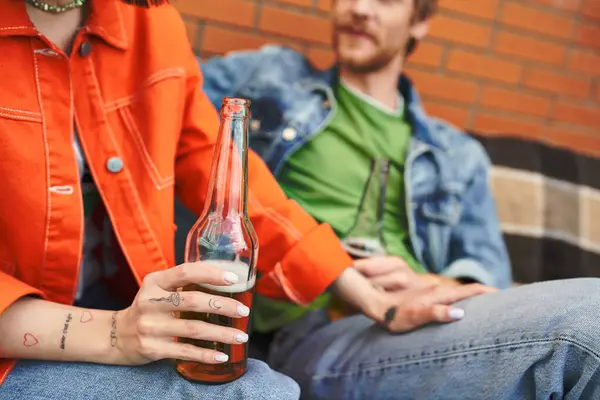 Um homem senta-se ao lado de uma mulher enquanto segura uma garrafa de cerveja, compartilhando um momento de relaxamento e conexão em um ambiente acolhedor. — Fotografia de Stock
