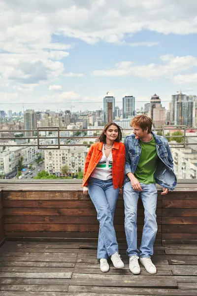 Ein Mann und eine Frau stehen triumphierend auf einem Wolkenkratzer und blicken mit einer Mischung aus Ehrfurcht und Stolz auf die Stadt darunter. — Stockfoto